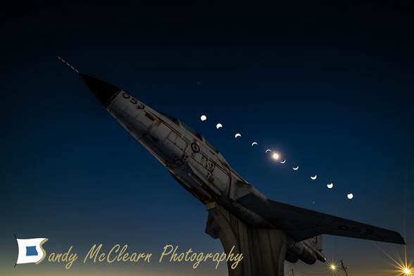 Composite image showing phases of a solar eclipse above an old fighter jet mounted on a concrete plinth.