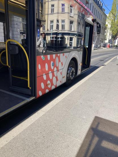 Zu sehen ist ein Bus bis zur Hintertür. Ein Altbau spiegelt sich im Busfenster und schafft die Illusion eines durchsichtigen Busses.