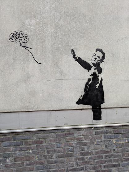 Foto eines Graffito am einer grauen Häuserwand. Zu sehen ist eine Abwandlung des Banksy-Graffitos des kleinen Mädchens, das einem davonfliegenden Herz-Ballon nachsieht. Hier ist der Kopf und ausgestreckte Arm von Elon Musk auf den Mädchenkörper montiert und es fliegt ein Gehirn-Ballon davon.