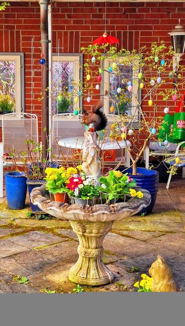 A squirrel eating a walnut on top of a fountain in front of colourful Easter decorations.