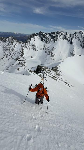 Man climbing in snow with crampoons and splitboard on back