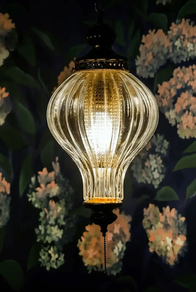 An ornate lamp against a floral wallpaper.