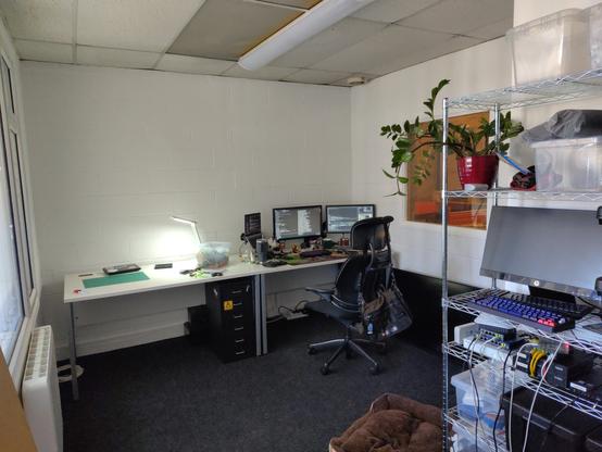 photograph of an office showing two desks, one "workbench" and one computer workstation.