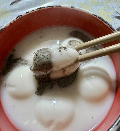 お椀に入った甘酒と湯圓。湯圓の1つを箸でつぶしており、中から灰色っぽくて黒いツブツブのある黒ゴマ黒蜜が溢れ出てます。