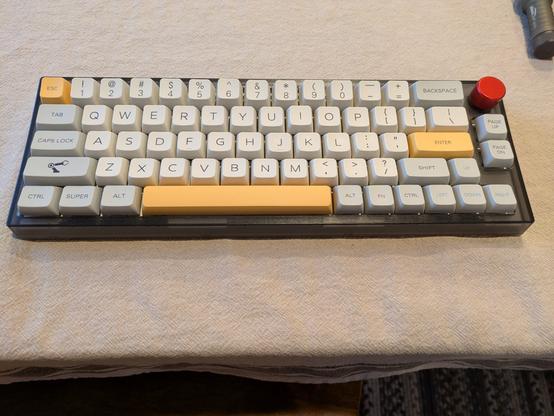 66 key mechanical keyboard in gray case with beige and light gray keys, yellow special keys and a red rotary knob.