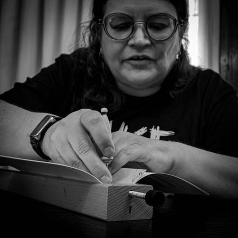 A Bookbinder's Apprentice punches holes on a music composition journal for sewing stations.