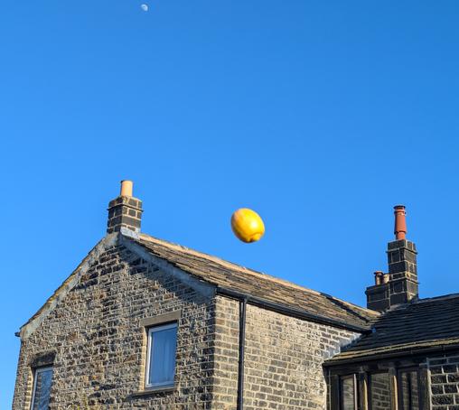 Moon and tossed lemon in a clear blue sky above a stone built Yorkshire farmhouse