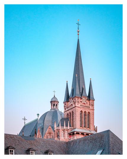 Aachen Cathedral featuring a prominent clock tower and clock against a clear blue sky.