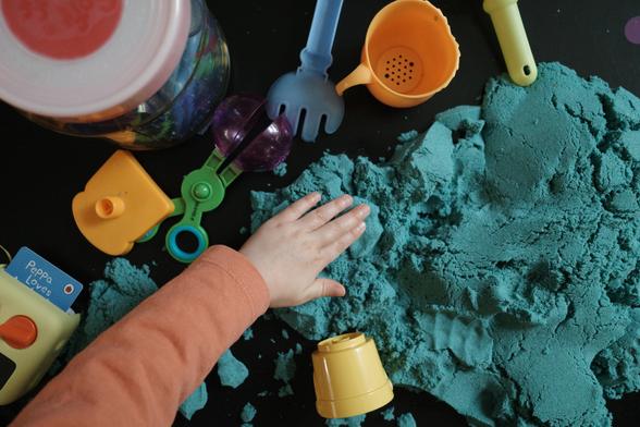 A child’s hand over some blue-coloured sand and some toys
