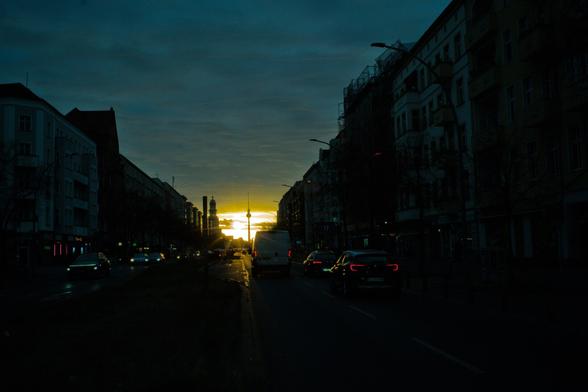 zwischen den Häusern durch fotografiert. Sonne dazwischen am untergehen. Dunkeles Bild. Bewölkung. Sonne Scheint durch.
