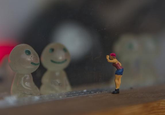 eine minifigur guckt durch eine scheibe und hebt dafür eine had zum kopf, hinter der scheibe zwei sitzende figuren die aliens sein könnten