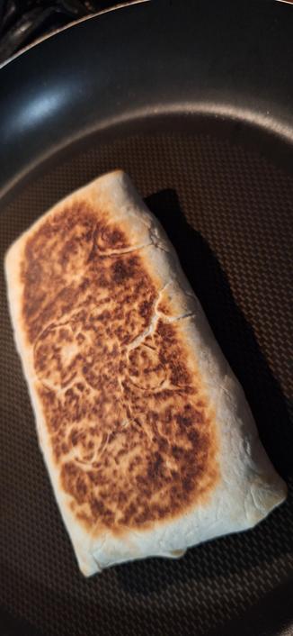 A homemade burrito-like object heating in a skillet.