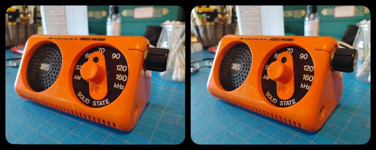 Stereoscopic, parallel view of a 1970s portable AM radio. It's bright orange, and prism-shaped, with a black circular dial that says "SOLID STATE" on the right and an identically-sized speaker grid on the left of one of the prism faces. It's got black volume knob on the upper right, triangular end.