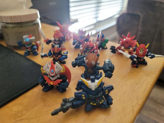 Twelve super robot wars gashapon miniatures, on the corner of my desk.  Starting in front and working towards the back, left to right, are

Huckebein MK3, a super robot wars original
Mazinkaiser and the Big O
Mazinger Z, Go Shogun, Daltanious, and Combattler V
Voltes V, Great Mazinger, God Mars, and Getter Dragon
and in the very rear, Shin Getter 1.
