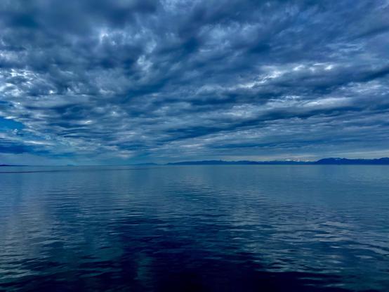 A landscape photo of the sea on a cloudy day. The photo has been edited to emphasize all the blues. There are ripples in the water, with touches of turquoise, and there are ripples in the clouds, with touches of white