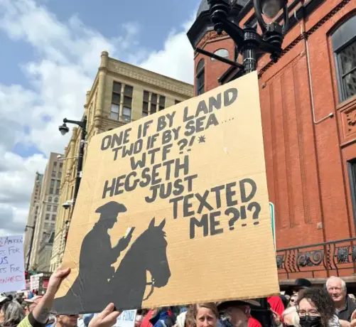 A protest sign that shows an silhouette of a man on a horse in a tricorn hat holding a cell phone, with the text, "One if by land, two if by see, WTF?! Hegseth just texted me!?"