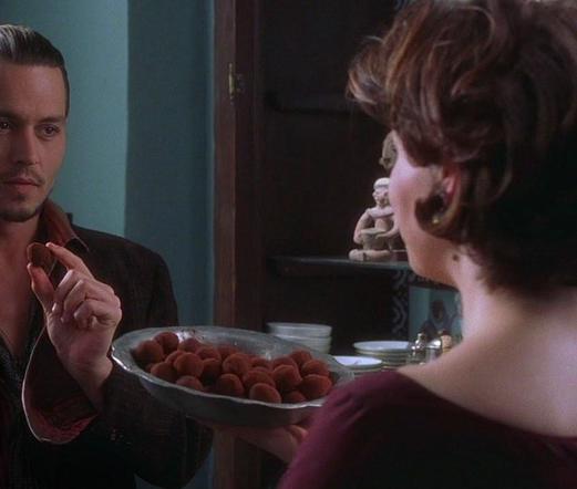 Johnny Depp taking a chocolate from a dish held by Juliette Binoche in a rustic shop