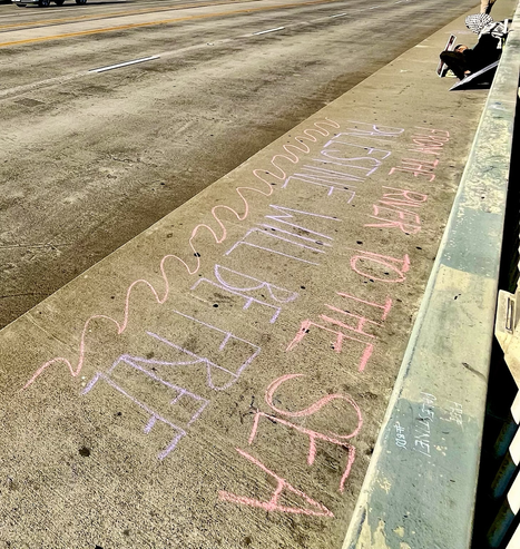 sidewalk chalk reads “from the river to the sea, palestine will be free,” figure in a keffiyeh sits nearby