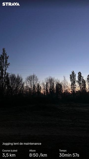 Chemin de terre bordé d’arbres sous un ciel partiellement éclairé par le soleil levant. Des statistiques Strava sont visibles.