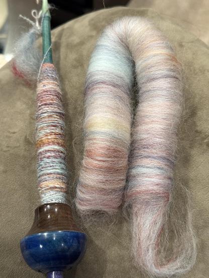 Supported spindle from Straddle Creek on the left, partial cop in place. Right, rolag with lace colors ranging from white to pink to blue