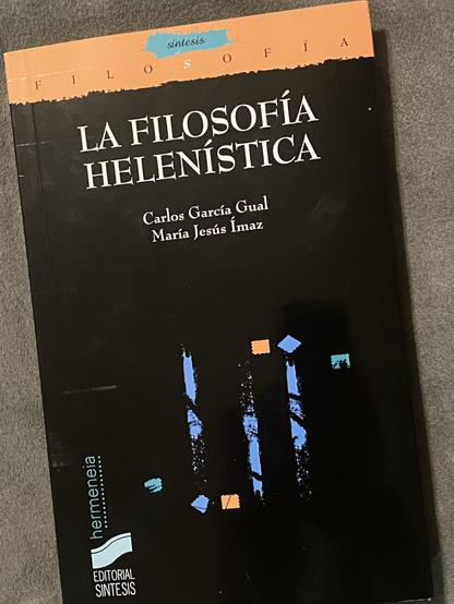 El libro La filosofía helenística apoyado sobre un cojín. La portada no tiene nada que destacar, es negra con unas pequeñas líneas de colores en el centro.