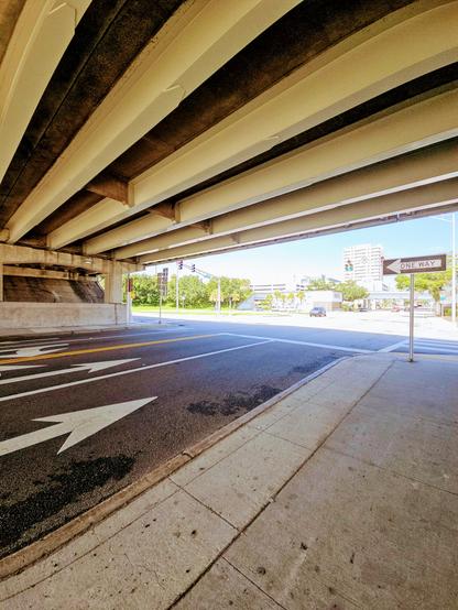 View beneath a highway bridge overpass. The section above where an interstate crosses over another roadway with colorful pavement signs.