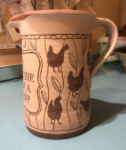 Photo of an unfired clay jug decorated using the sgraffito technique with chicken and plant motifs. Left side.