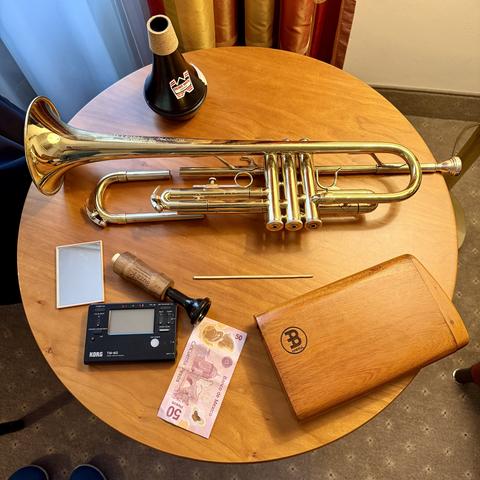 Im Hotelzimmer. Eine Trompete, ein Übedämpfer, Metronom, Posaunenmundstück, Didgeridoo, Geldschein und Handspiegel.