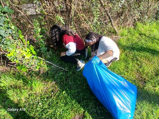 Bi gazte errekondoko zaborra batzen, plastikozko zabor-poltsa urdina betetzen.
