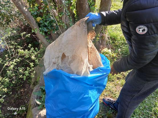 Gazte bat errekondoan batutako zaborra erakusten eta plastikozko zabor-poltsa urdinean sartzen.