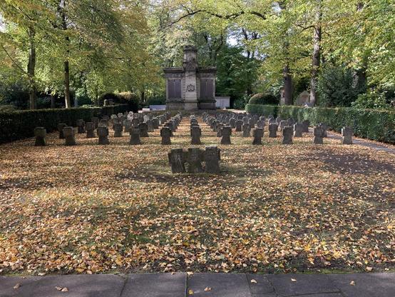 Auf dem Melaten-Friedhof in Köln: Drei Steinkreuze, die miteinander verbunden sind. Sie stehen auf einem Gräberfeld für Opfer des Zweiten Weltkriegs und erinnern an drei Mitglieder eines Bombenräumkommandos.
