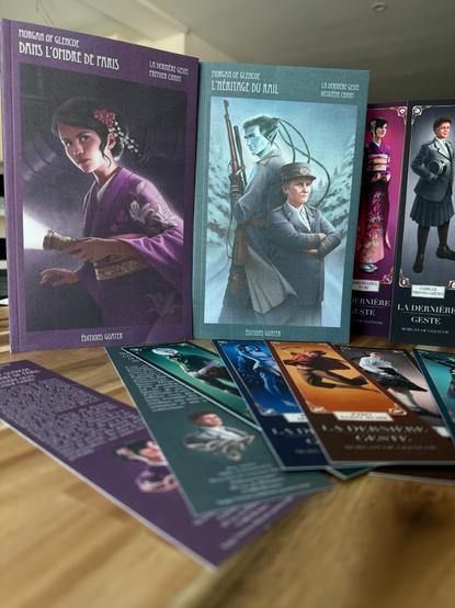 Deux premiers tomes de La dernière veste avec des marques pages à l’effigie des personnages. La couverture du premier montre Yuri, en kimono japonais mauve dans un souterrain, lampe à la main. La couverture du second montre la capitaine Trente-chêne et Alcyone (peau bleu et longues tresses, fusil en main) dos à dos dans leur uniforme du rail.