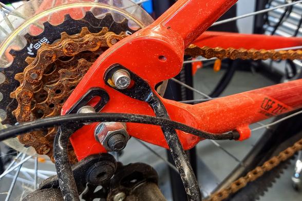 Détail d'un vélo, centré sur la transmission au niveau de la roue arrière. Le vélo est de couleur rouge, la chaine et les pignons sont pétris de rouille avec ses tons ocre roux, assortis à la couleur du vélo.