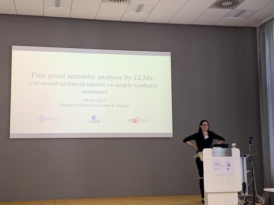 Maarouf (a woman dressed in black, arms akimbo) in front of her title slide