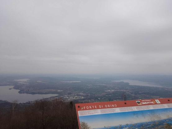 Punto panoramico a 1139 mt da cui si vedono i laghi della provincia di Varese. Cielo molto nuvoloso, foschia all'orizzonte, in un angolo quasi in primo piano si nota il cartello con la scritta "Forte di Orino" e la foto del punto panoramico con legenda