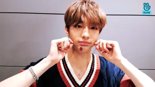 Hyunjin holds the necklace with I.N's red oval pendant under his lower lip