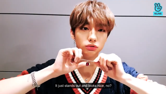 Hyunjin during a livestream, holding up I.N's red oval pendant yet again. Caption: "It just stands out and looks nice, no?"