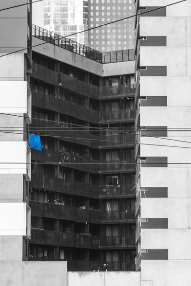 A black and white photo of a white building facade with recessed black balconies, one of which has a brilliant blue sheet hanging from it