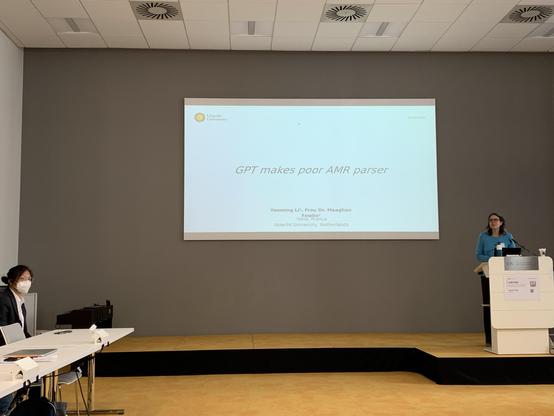 Fowlie standing behind the lectern, Li sitting, in front of their title slide
