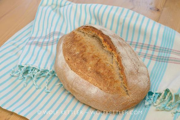 A rustic loaf of bread on a piece of white fabric with turquoise stripes.