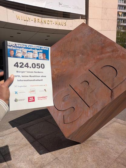 Eine Person hält die gebundene Unterschriftenliste der 424.050 Unterzeichner*innen der Petition "SPD, keine Koalition ohne Informationsfreiheit" vor dem Willy-Brandt-Haus, der Parteizentrale der SPD, in der Hand.