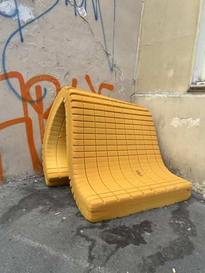 A yellow foam mattress folded into a graffiti-filled street corner.
