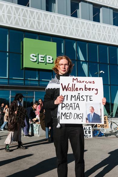 A protester with a placard saying: "Marcus Walleberg vi måste prata med dig".