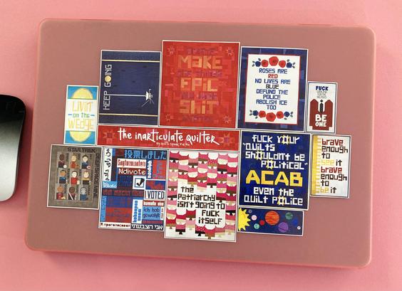 A bunch of quilt stickers on a pink laptop cover. The quilts are all different color schemes and designs but they almost all have pieced letters and look like one person could have made them all (namely me, The Inarticulate Quilter)