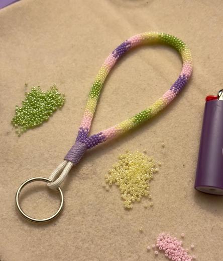 A bead wrapped wristlet keychain in purple, light pink, buttery yellow, and green

The wristlet is sitting on a bead mat with green, yellow, and pink seed beads, and a purple lighter