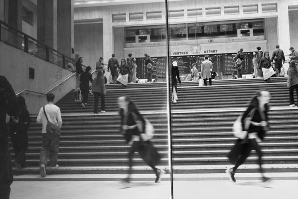Before a wide stair case, a woman and her reflection seem to be running in two different directions.