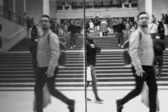 Before a wide stair case, a man and his reflection seem to be looking for something in two different directions.