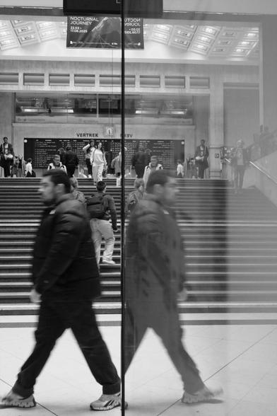 Before a wide stair case, a man and his reflection seem to be striding in two different directions.