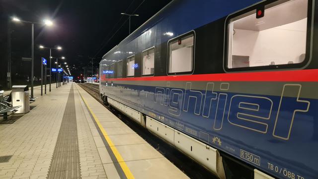 A blue ÖBB Nightjet train waiting at night at an empty platform. The “Nightjet” wordmark clearly visible on the side.