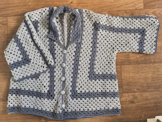 A light blue, crocheted men's button up shirt with collar. There are darker blue accents on the collar, edging and 2 dark blue stripes that follow the shape of the body. It is made using a granny hexagon shirt pattern, self designed.